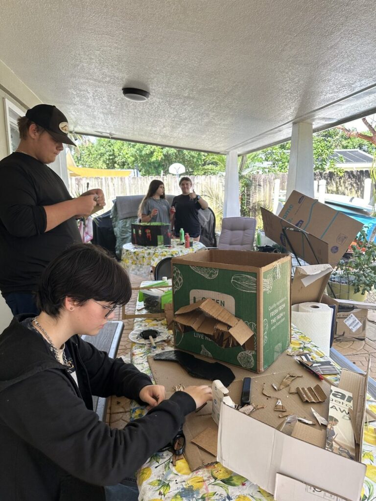 Students build with cardboard and tape on the covered patio