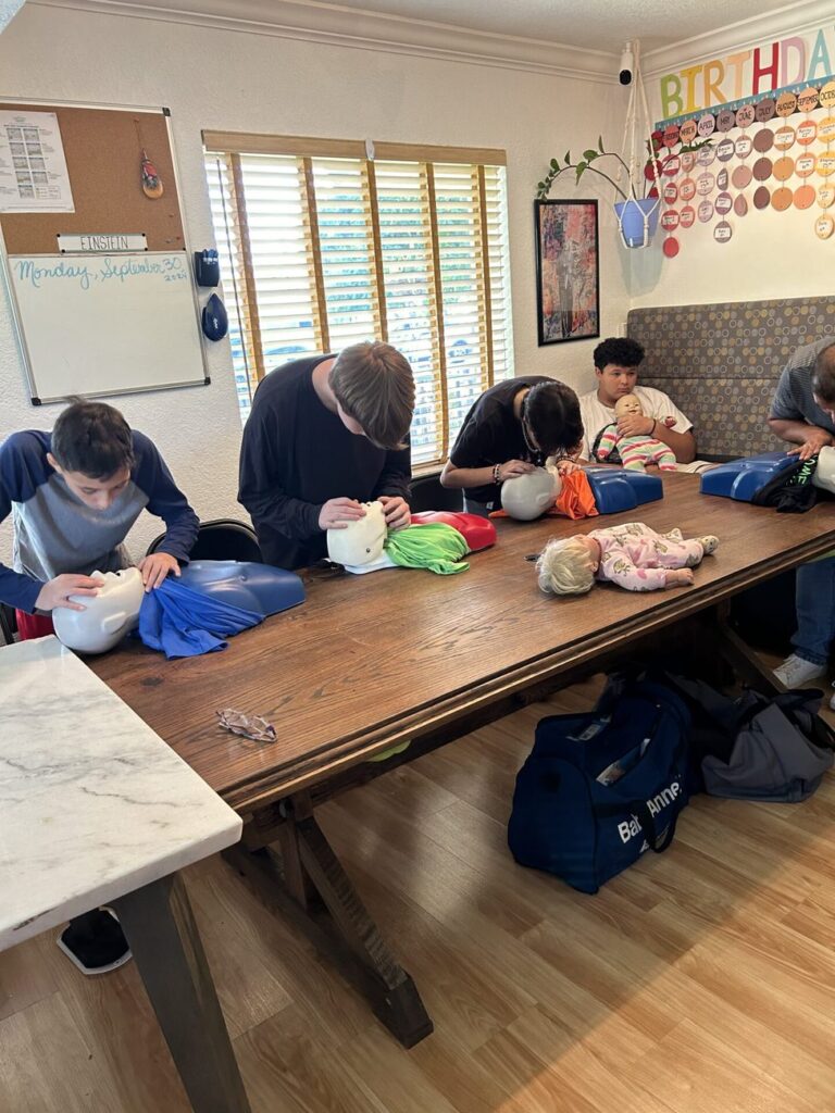 Students practice CPR on infant and adult training manikins at a long table