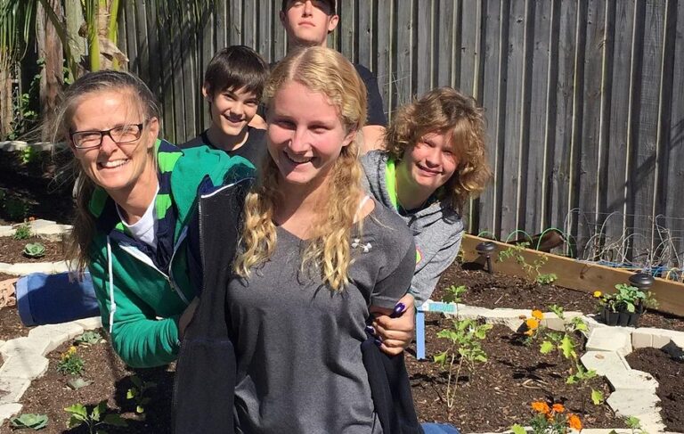 Smiling students and a teacher pose in a vegetable garden