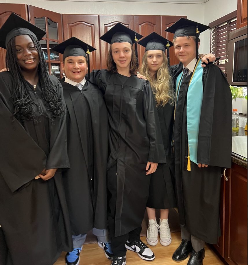 Five graduates in black caps and gowns smile together