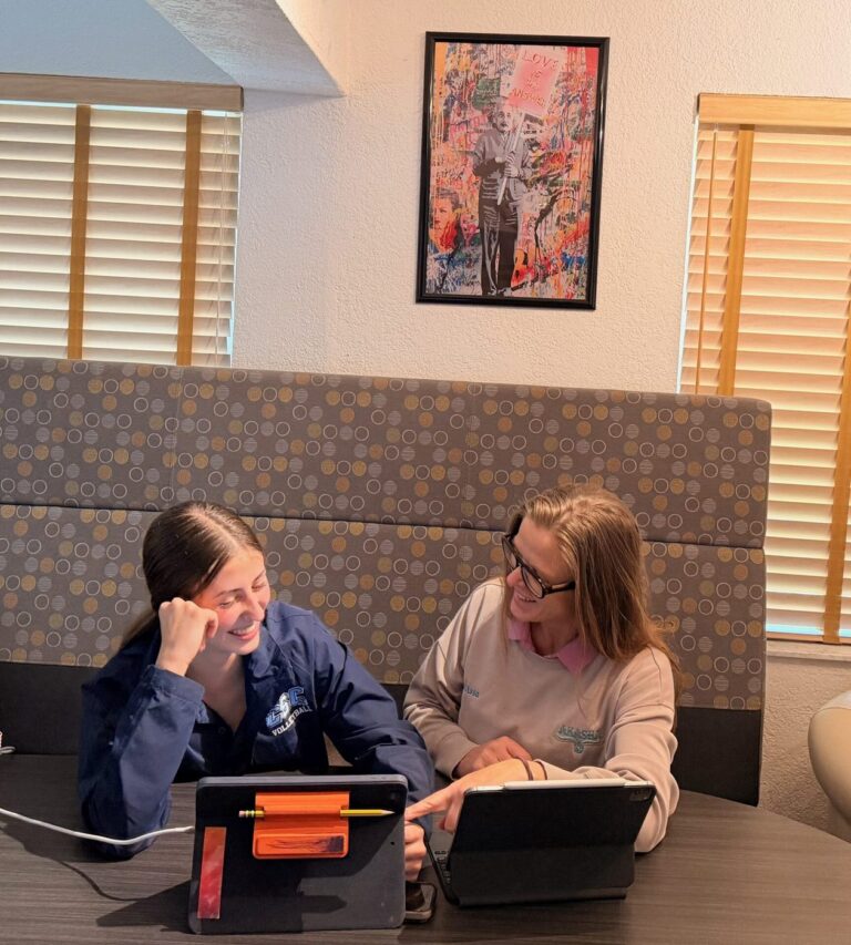 Two smiling students share a booth, each working on a tablet