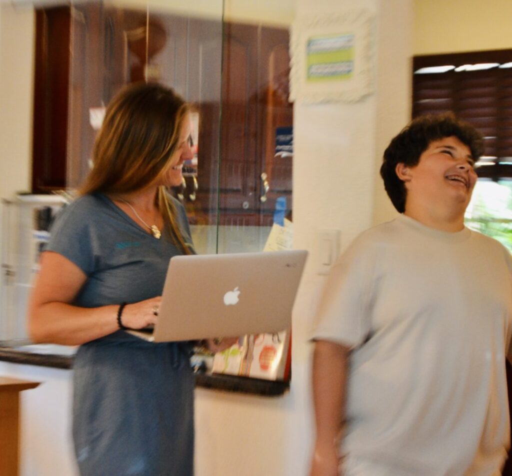 A teacher holding a laptop laughs with a student