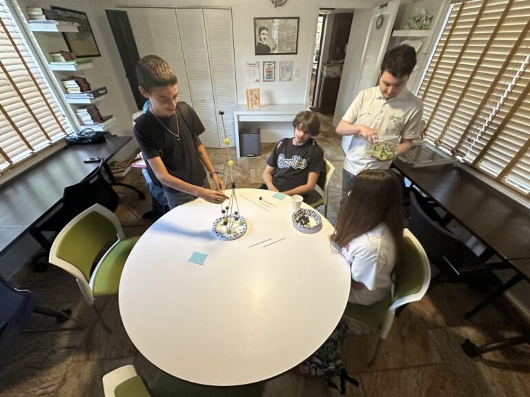 Students gather around a round white table for a hands-on project