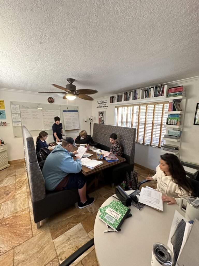 Students study at booths and tables in a bright room lined with bookshelves